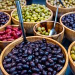 Various types of olives displayed in wooden bowls at an outdoor market.